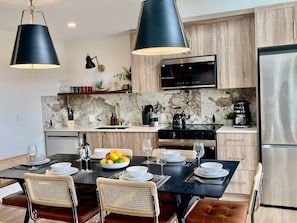 A modern kitchen with a marble backsplash, wooden cabinets, a stainless steel refrigerator, and a dining area with a black table and wicker chairs. - RETRORIDGE - DOWNTOWN - ROOFTOP HOT TUB (Canmore)