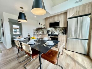 A modern kitchen with a dining area, stainless steel appliances, and a flat-screen TV. - RETRORIDGE - DOWNTOWN - ROOFTOP HOT TUB (Canmore)