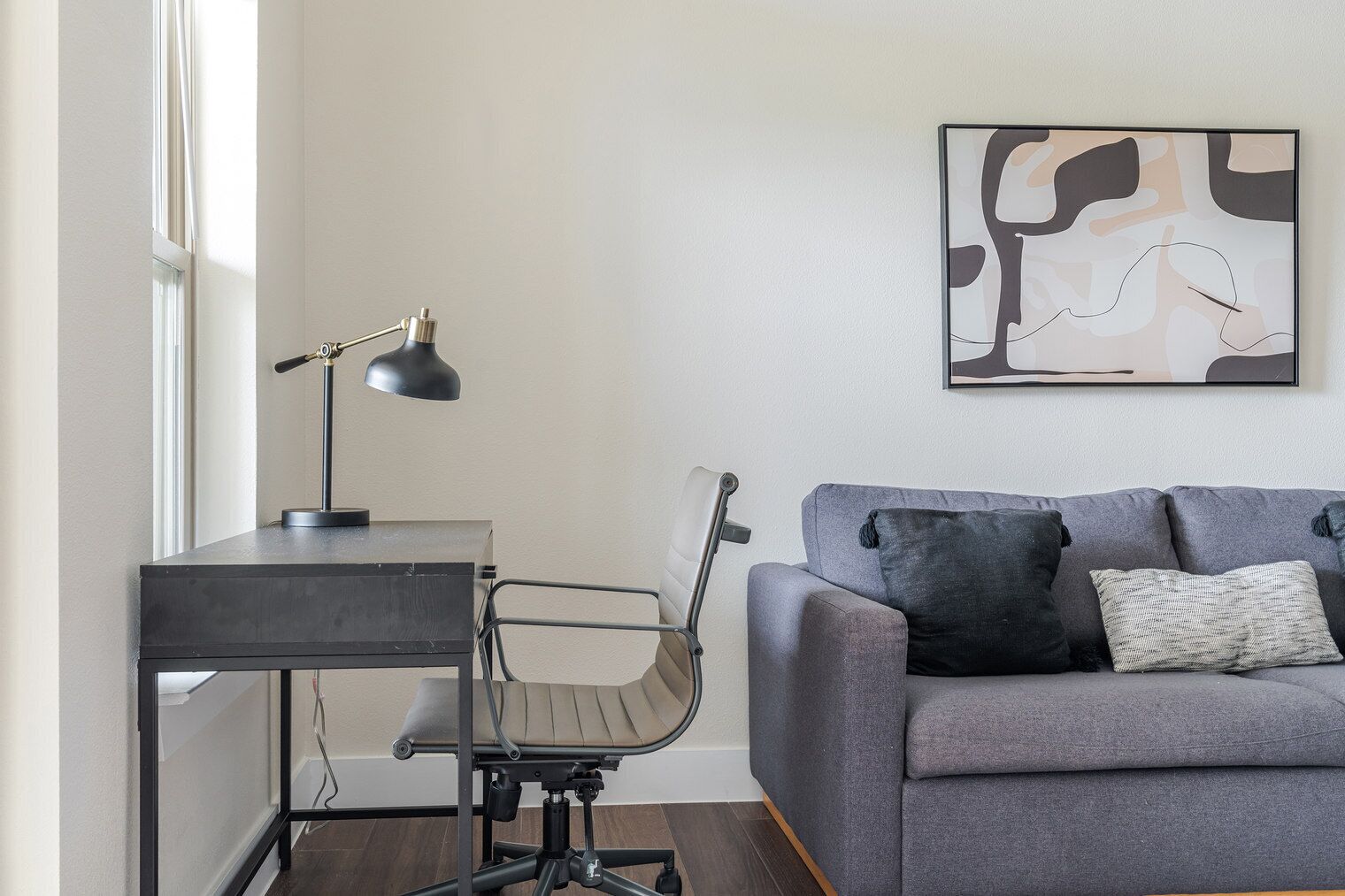 Una sala de estar moderna con un escritorio, una silla y un sofá gris con almohadones.