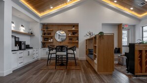 A modern kitchen with white cabinetry, wooden shelves, and a dining area with a round mirror and two chairs. - Blueground | Scofield Farms, pool, nr Walnut Creek Park (Austin)