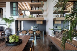 Une cuisine moderne avec des étagères en bois, un coin repas doté d’une grande table et de chaises, et une vue sur la ville.
