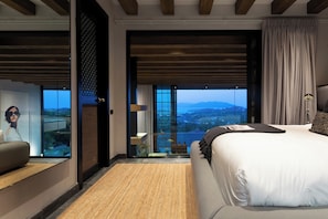 A modern hotel room with a large bed, a seating area, a view of the outdoors, and a sliding door leading to a balcony. - Villa Sierra (Koh Samui)