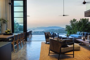 Un intérieur moderne comprenant un coin repas, des sièges et une grande fenêtre offrant une vue sur les montagnes et un plan d’eau.