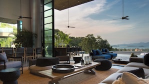 A modern living area with a large window, ceiling fans, and outdoor seating. - Villa Sierra (Koh Samui)
