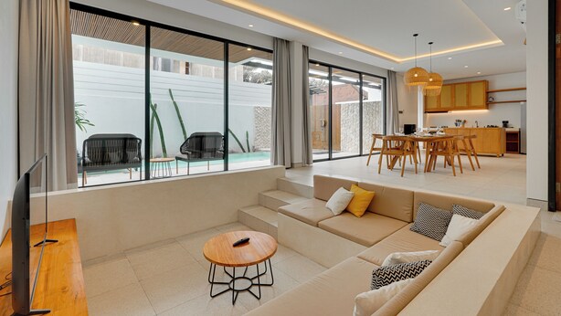 A modern living room with a sofa, a coffee table, and a TV. There is a dining area with a table and chairs. - Villa RHYS - Canggu (Canggu)