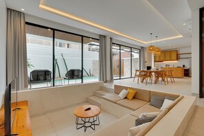 Een moderne woonkamer met een bank, een salontafel en een televisie. Er is een eethoek met een tafel en stoelen.