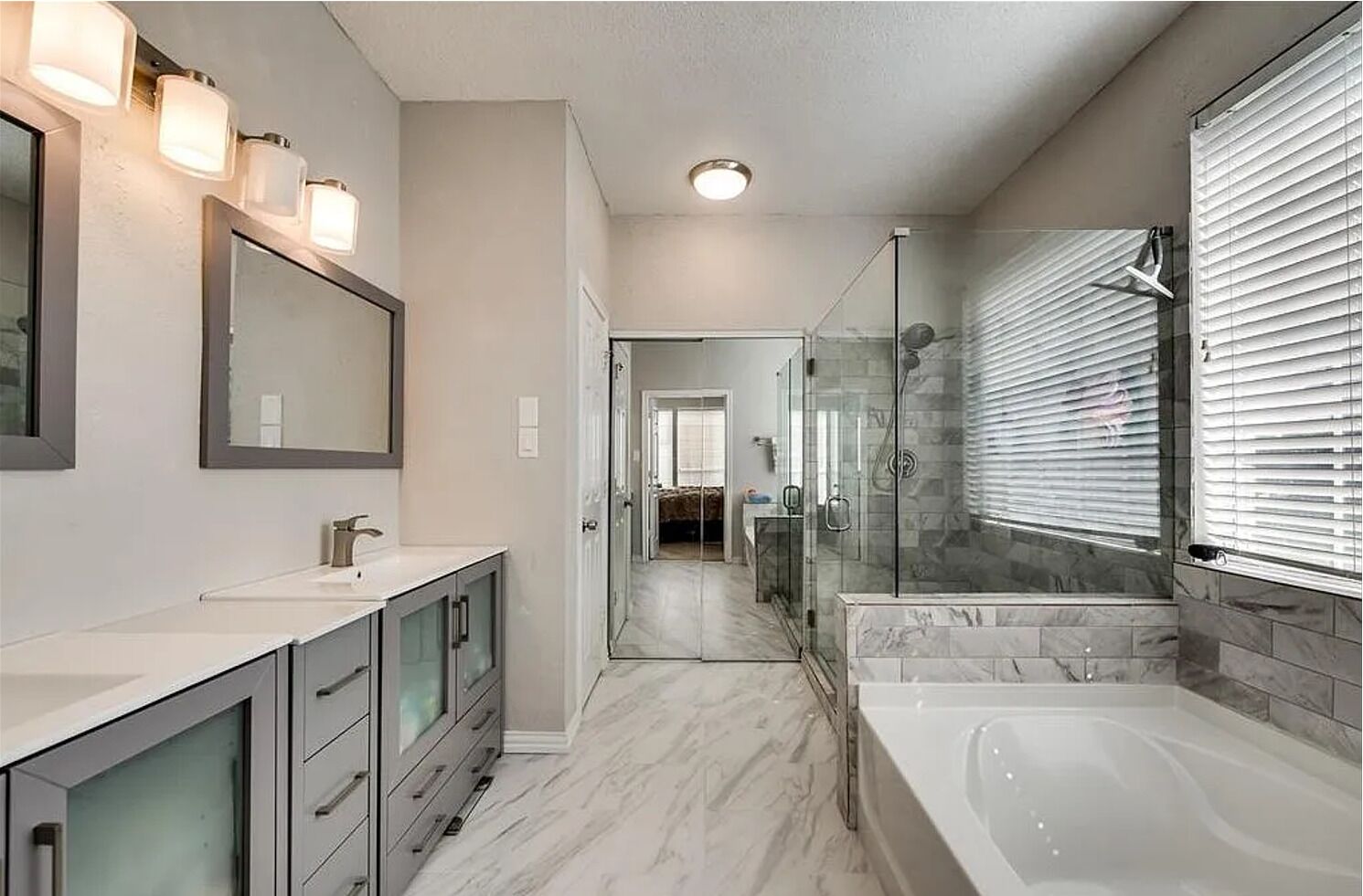 A modern bathroom with a glass-enclosed shower, a large bathtub, and a vanity with a mirror and lights.
