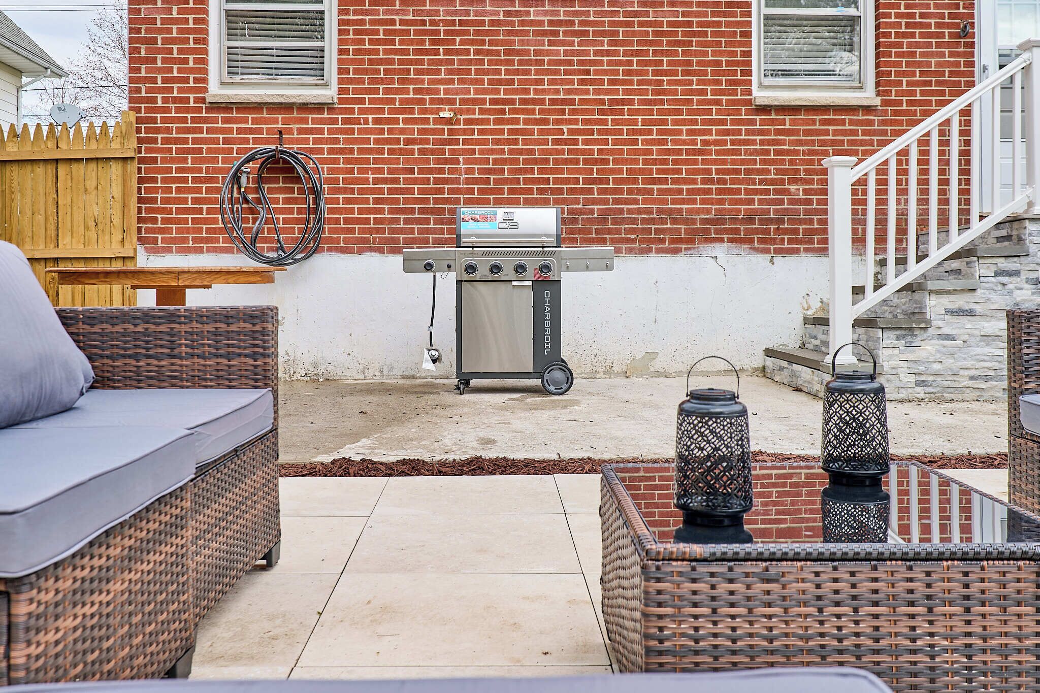 A patio area with wicker furniture, a grill, and a brick house in the background.