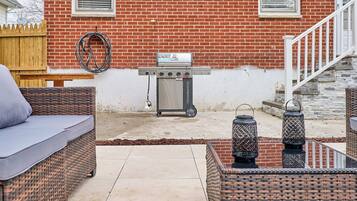 A patio area with wicker furniture, a grill, and a brick house in the background.