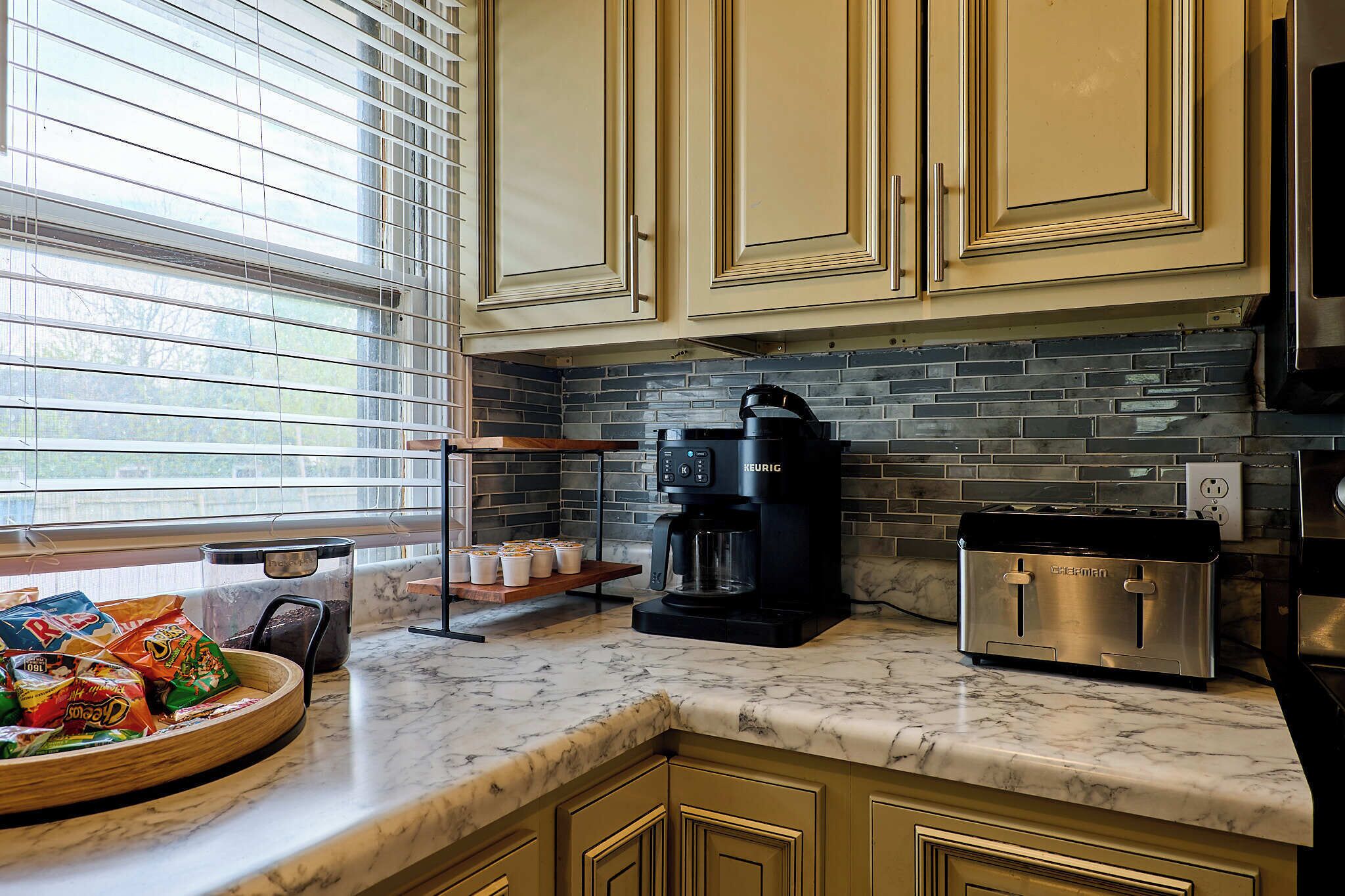 A kitchen with a coffee maker, toaster, and a window with blinds.