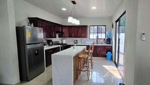 A modern kitchen with a marble island, dark wooden cabinets, stainless steel appliances, and a large window providing natural light. - Just 5-minutes away to the beach. Spacious 5-bedroom house at Costa Azul,Metalio (Metalio)