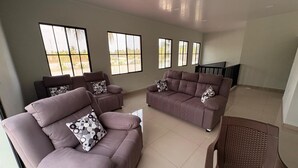 A spacious living room with a brown sofa set, patterned cushions, and large windows offering a view of palm trees. - Just 5-minutes away to the beach. Spacious 5-bedroom house at Costa Azul,Metalio (Metalio)