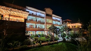Ein mehrstöckiges Hotel mit Balkonen, einem gepflegten Garten und Blick in der Nacht.