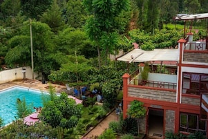 A pool surrounded by lush greenery, a two-story building with a red and white facade, and a staircase leading to the upper level.