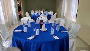 Ein Konferenzraum mit runden Tischen, die mit blauen Tischdecken bedeckt sind, weißen Stühlen und Wasserflaschen.