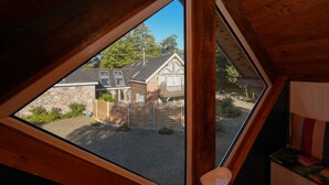 Et værelse med træloft, et vindue der ud til et hus og en have, samt en træbænk med pude.