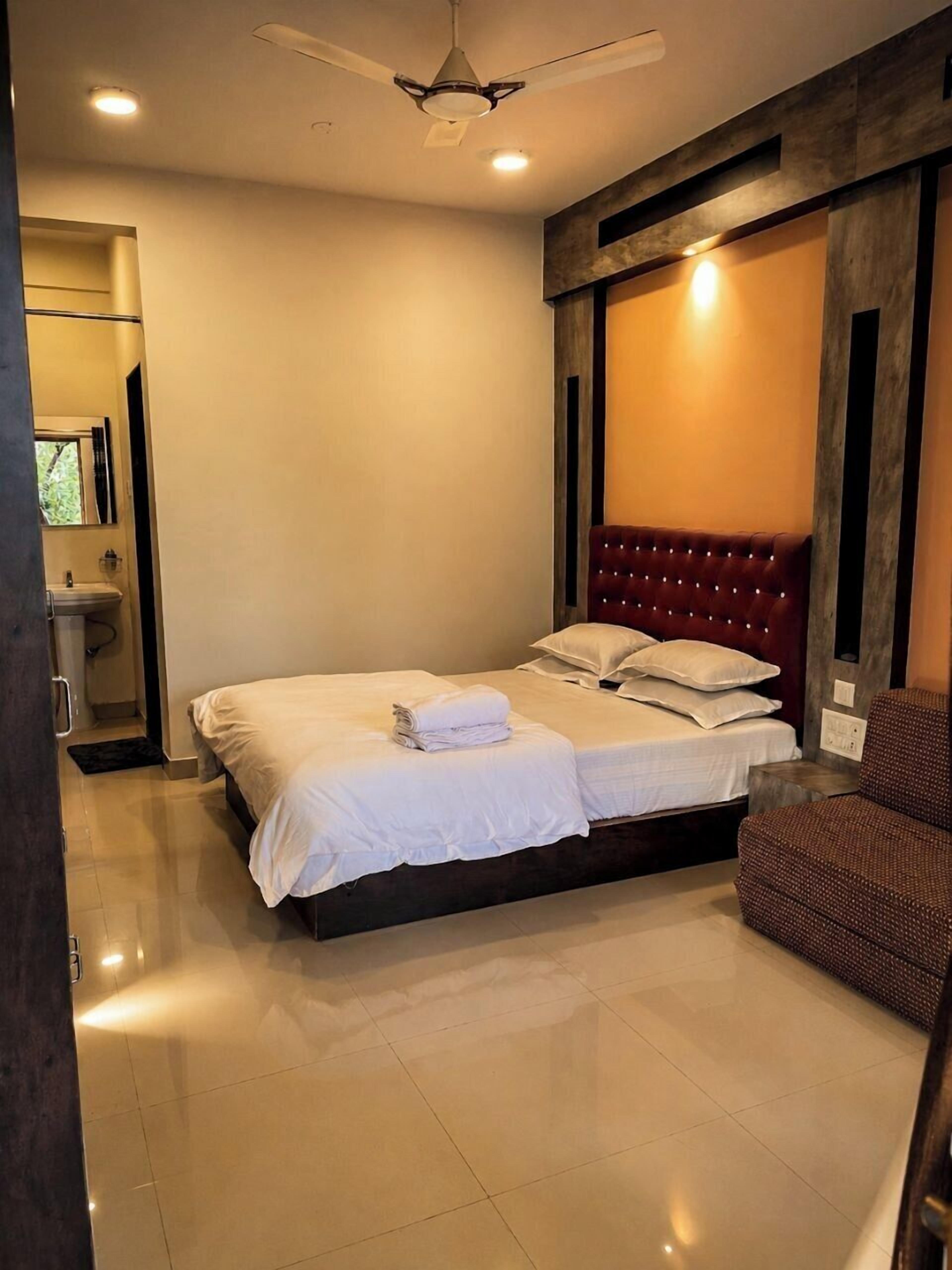 Un dormitorio moderno con una cama grande, una silla, un ventilador de techo y un baño visible a través de una puerta abierta.