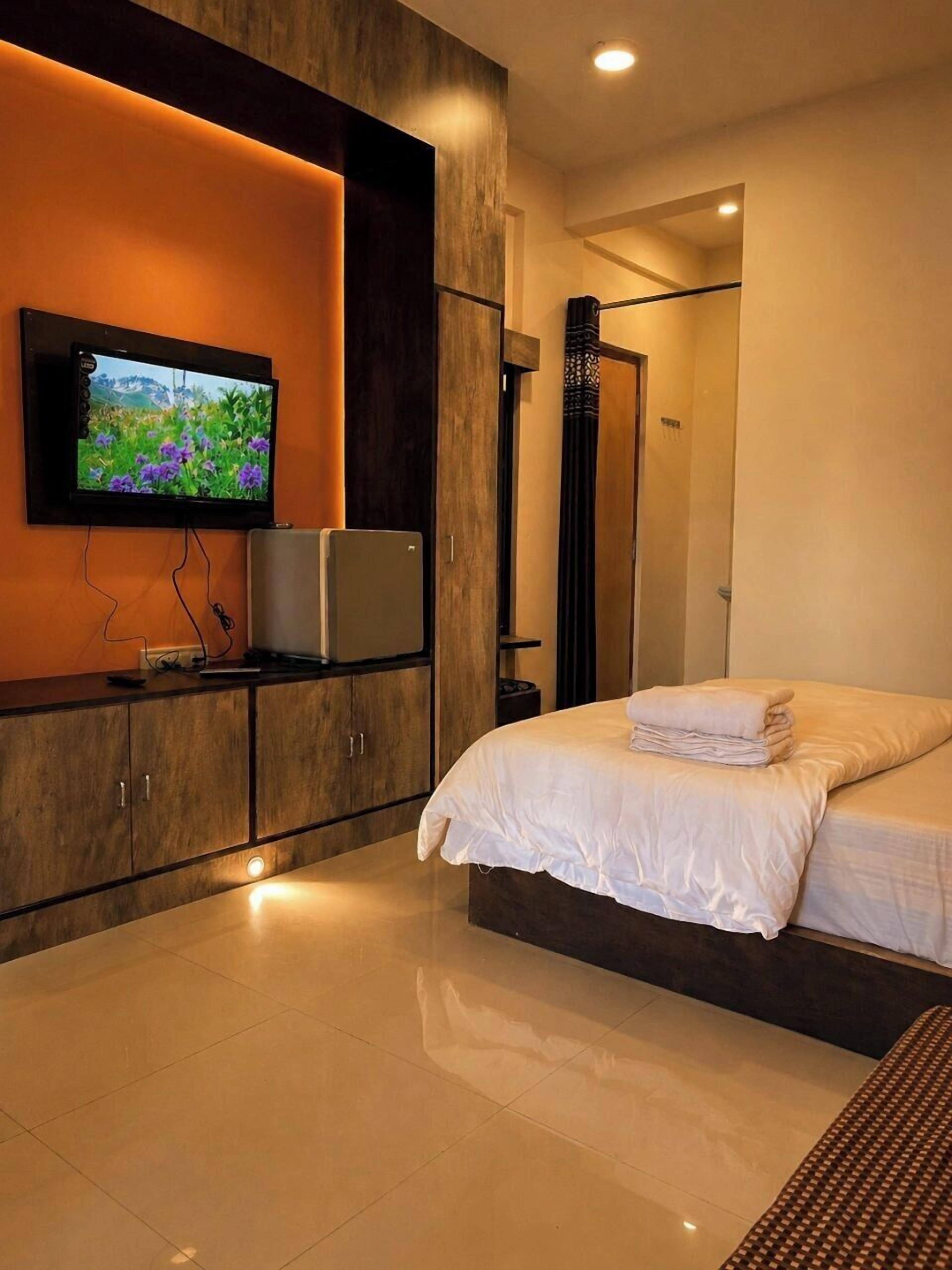 Un dormitorio moderno con televisión de pantalla plana en la pared, cama con ropa de cama blanca y armario empotrado.