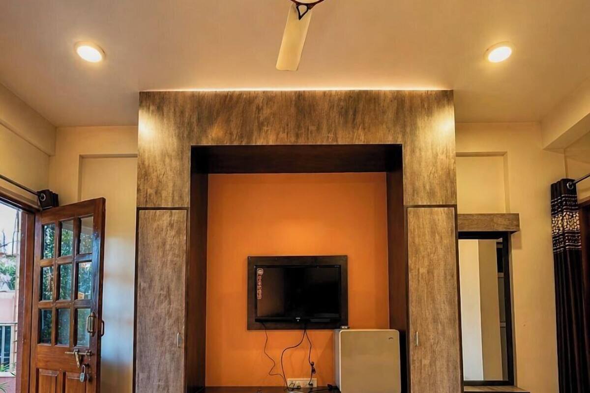 Une chambre à coucher comprenant un lit, un téléviseur, un ventilateur de plafond et une armoire en bois.