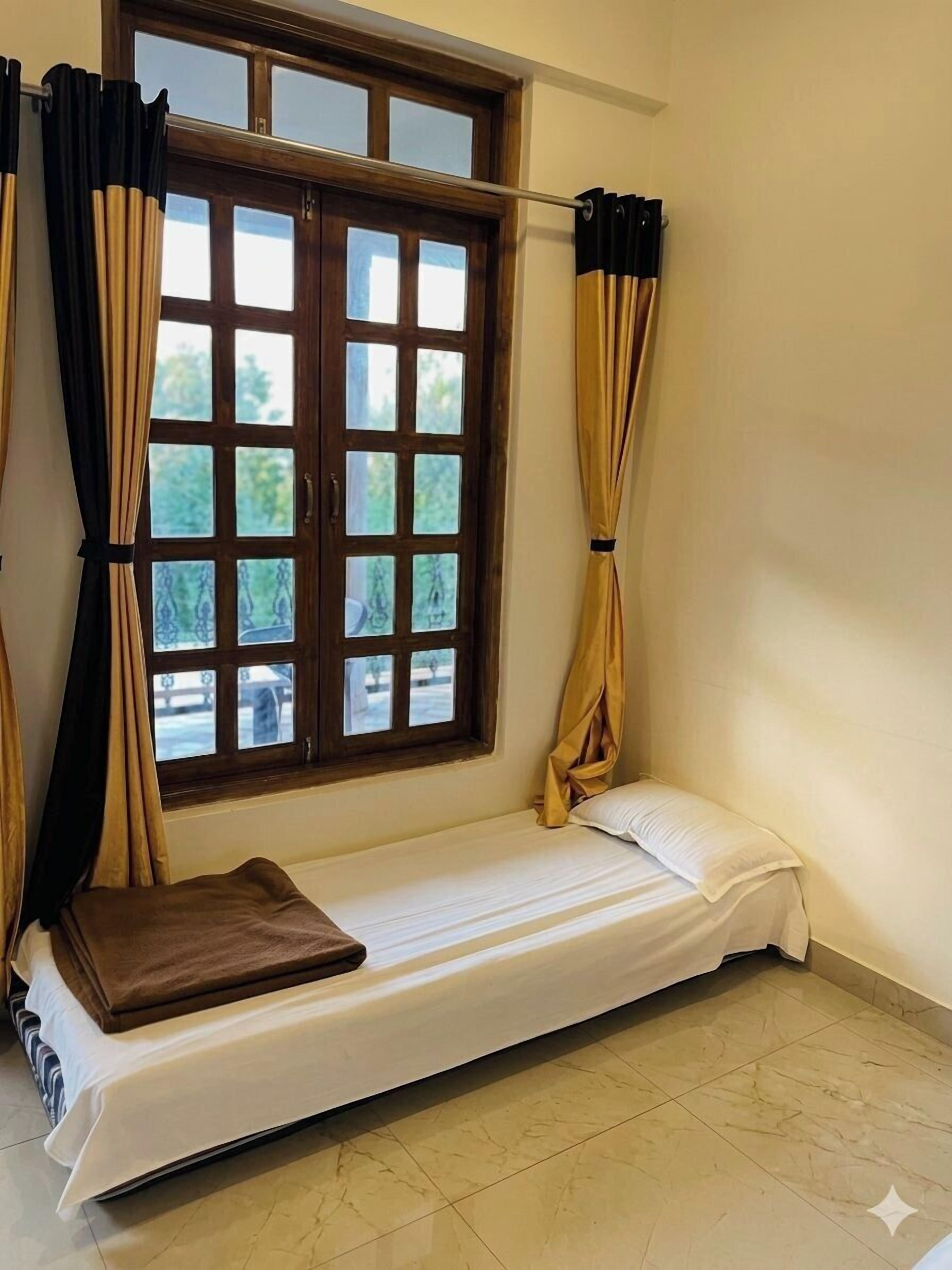 Un lit simple avec une tête de lit en bois, une fenêtre donnant sur un paysage verdoyant et des rideaux.