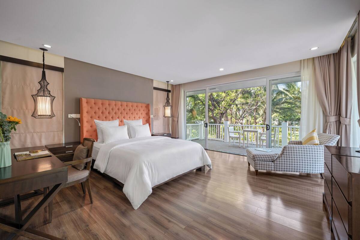 Un dormitorio con una cama grande, una mesa de comedor, un balcón con mobiliario exterior y vistas al verdor.