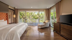 A bedroom with a large bed, a TV, a balcony with a table and chairs, and a view of greenery. - Pool Villas Resort (Da Nang)