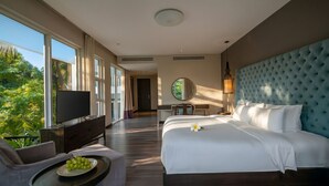A hotel room with a large bed, a TV, a desk, and a view of greenery. - Pool Villas Resort (Da Nang)