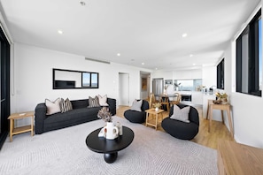 A modern living room with a sofa, coffee table, and a dining area with chairs. - Panorama by Khove (Surfers Paradise)