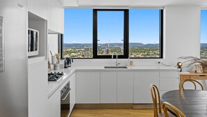Een moderne keuken met een groot raam, witte kasten en een eethoek met een tafel en stoelen.