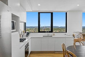 A modern kitchen with a large window, white cabinetry, and a dining area with a table and chairs. - Panorama by Khove (Surfers Paradise)