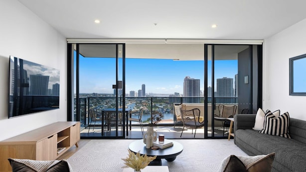 Een moderne woonkamer met uitzicht over de stad, een flatscreen televisie, een bank, een salontafel en een balkon met zitplaatsen.