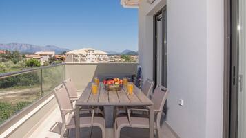 Un balcon avec une table et des chaises, une porte vitrée et une vue sur des immeubles et des montagnes.