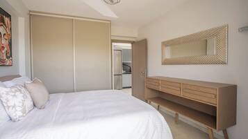 Une chambre à coucher avec un lit, une armoire, un miroir et, au fond, un coin cuisine.