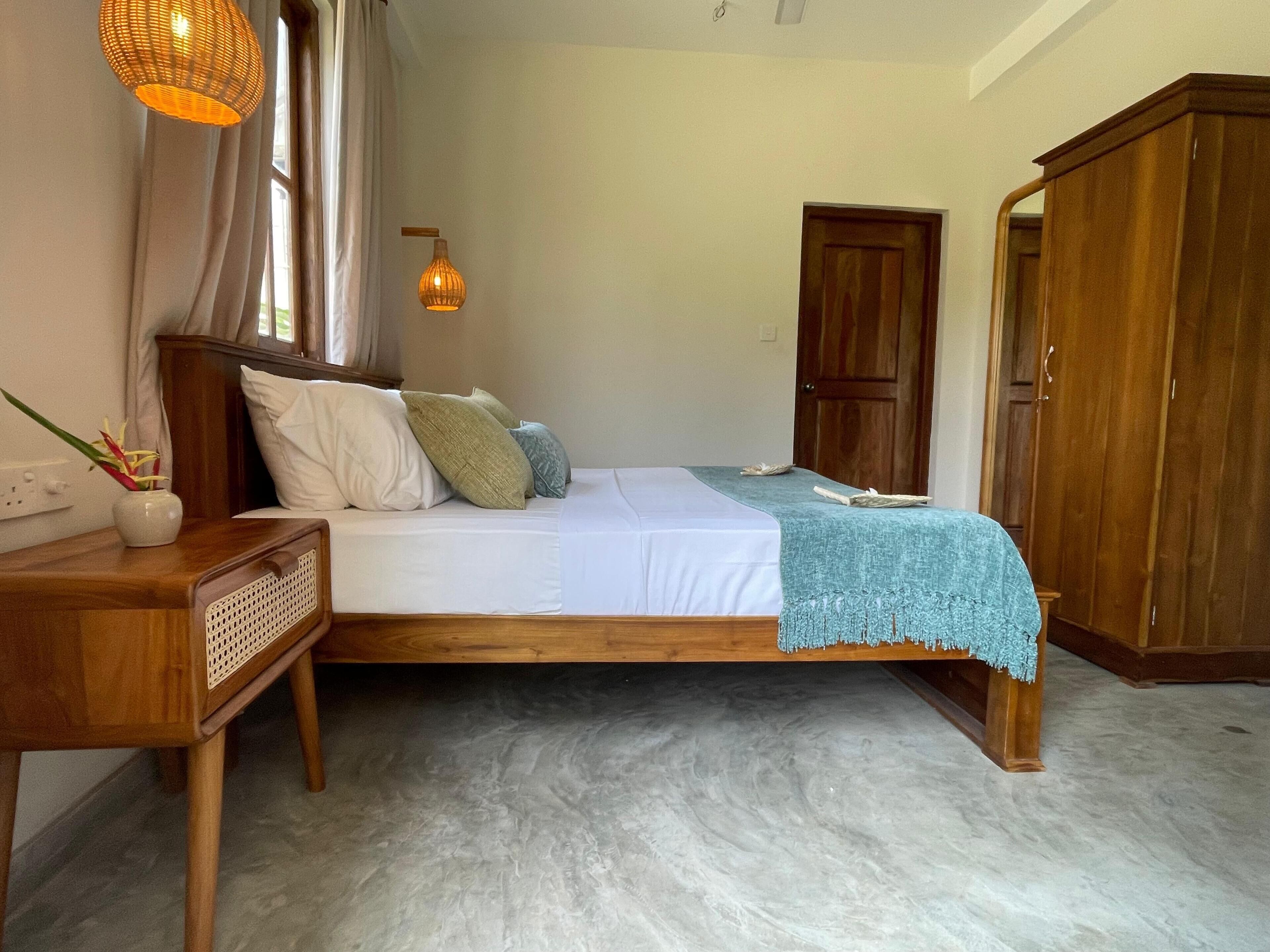 A bedroom with a wooden bed, a bedside table, a lamp, a wardrobe, and a window with curtains.
