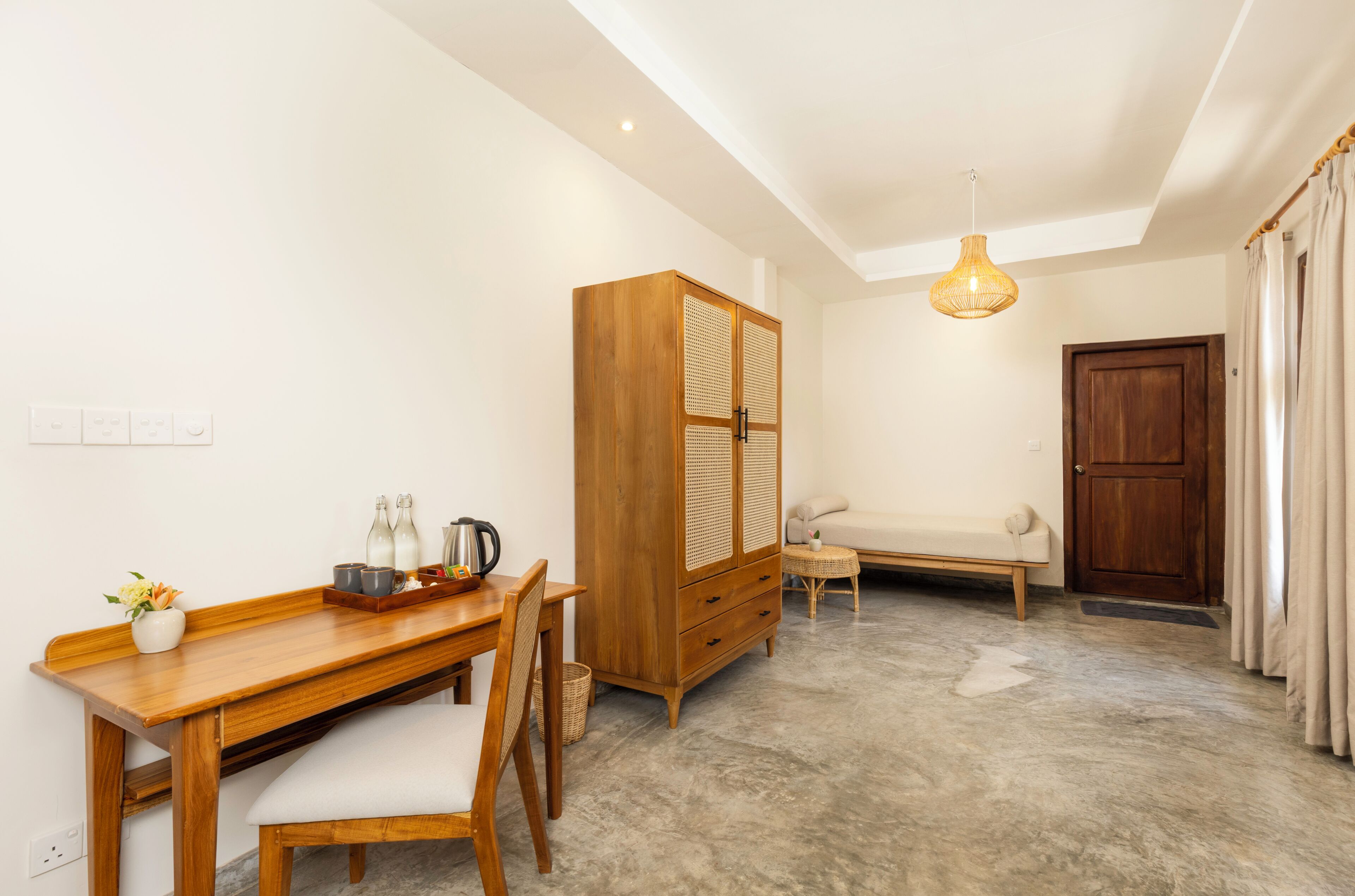 A room with a wooden desk, a cabinet, a sofa, and a hanging light fixture.