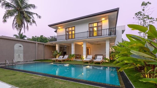 Una casa de dos pisos con piscina, un balcón con mobiliario exterior y un césped bien cuidado.