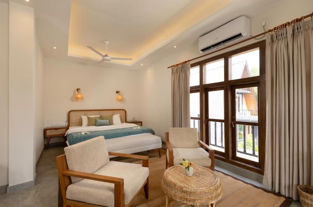 A hotel room with a bed, two chairs, a small table, and a large window with curtains.