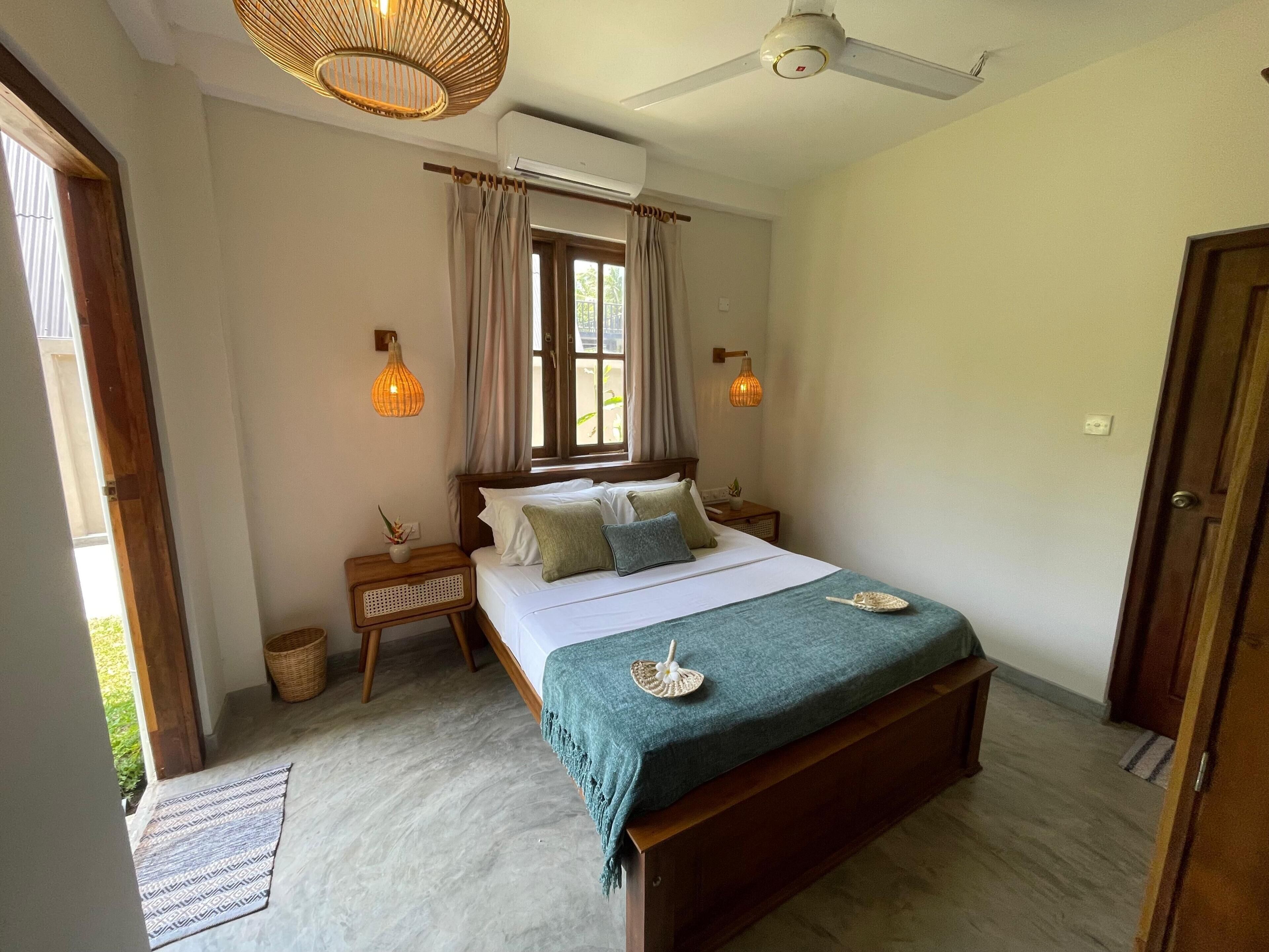 A bedroom with a bed, bedside tables, a window with curtains, a ceiling fan, and an air conditioning unit.