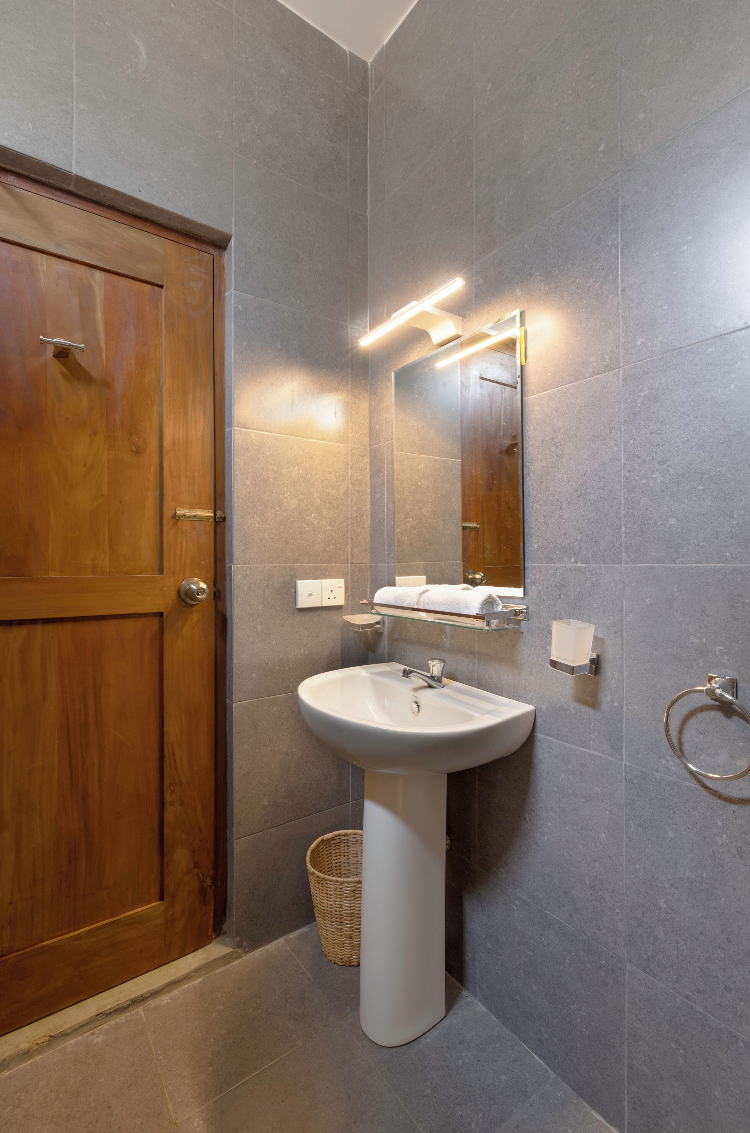 A bathroom with a wooden door, a pedestal sink, a mirror, and a towel rack.