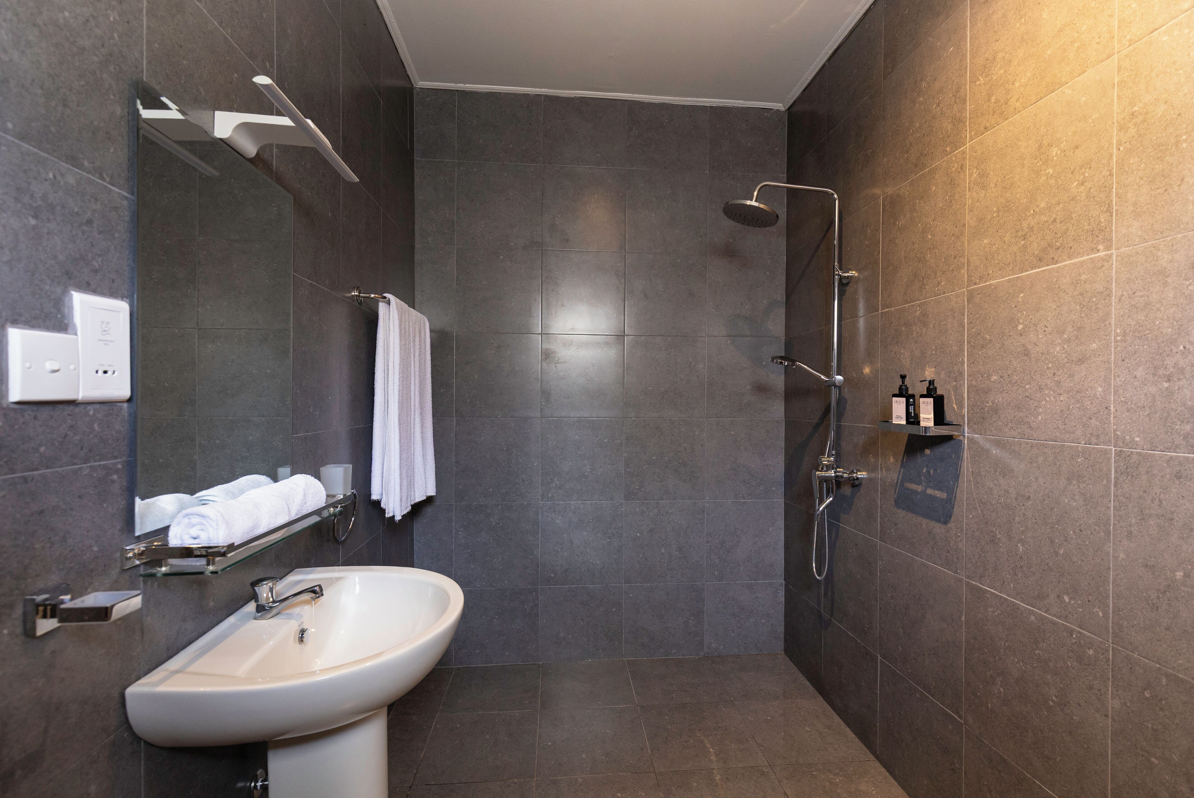 A modern bathroom with a sink, mirror, towel rack, shower, and toiletries.