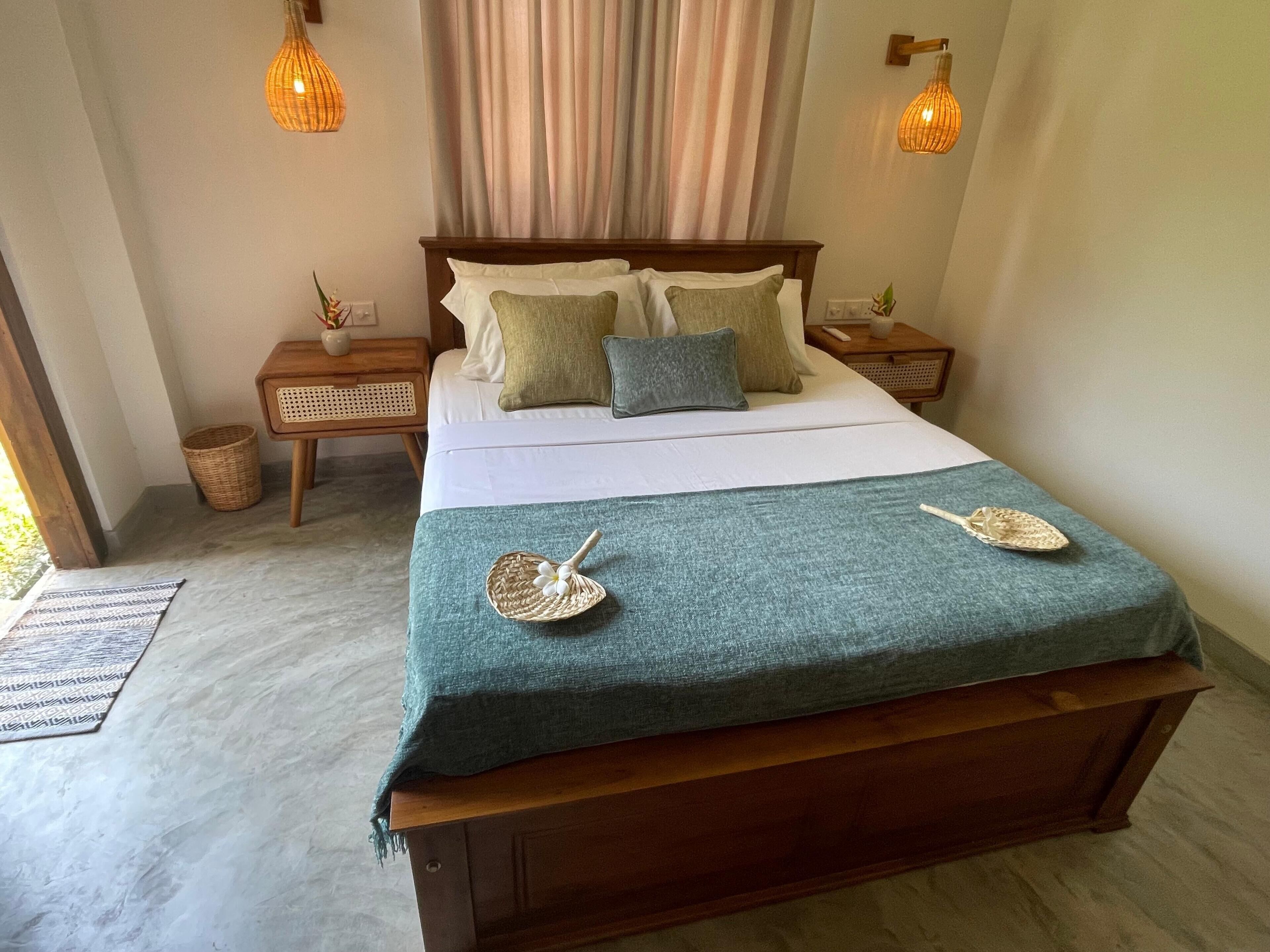 Una cama bien hecha con un edredón verde, dos lámparas de noche y una mesita de noche con una planta.