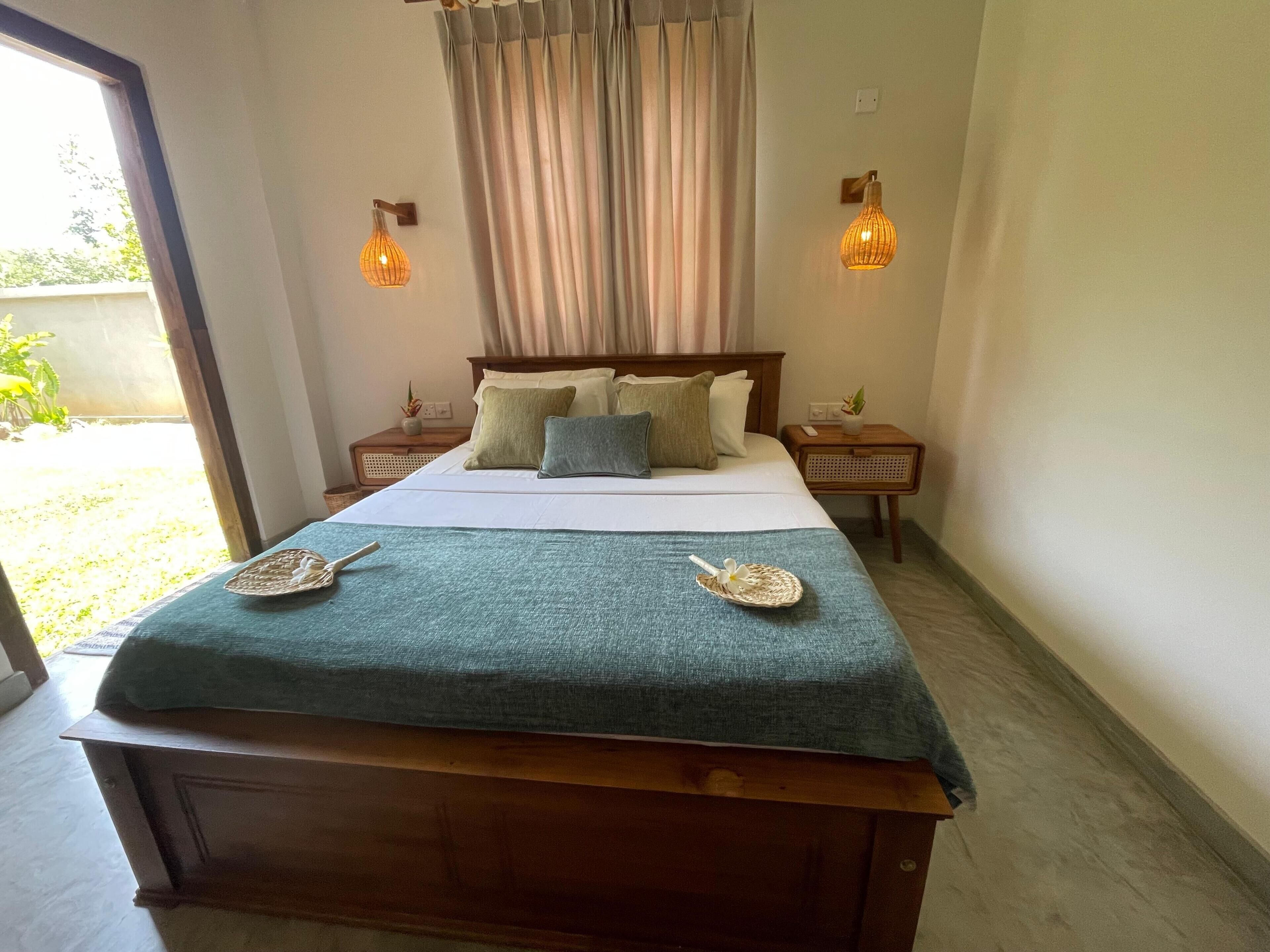 A neatly made bed with a blue blanket, two bedside tables with lamps, and a view of the outdoors through a door.