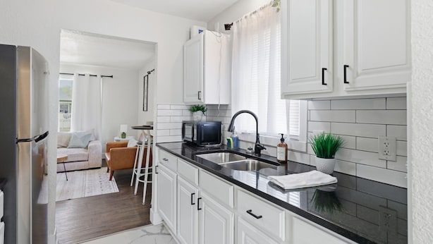 Una cucina moderna con mobili bianchi, un piano di lavoro nero e un frigorifero in acciaio inossidabile.