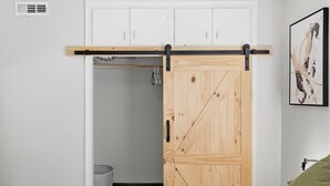 Una stanza con una porta a battente in stile cascina, mobili bianchi, una parete bianca e un quadro astratto incorniciato.