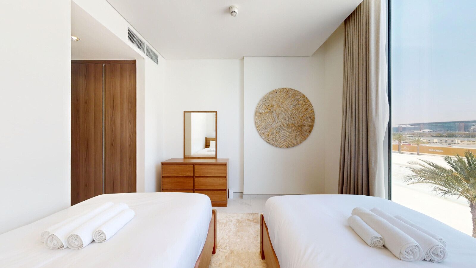 Habitación de hotel con dos camas, un aparador de madera, una obra de arte redonda en la pared y vistas de la ciudad.
