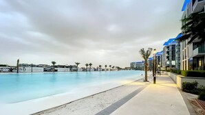 Una piscina con un paseo, palmeras y edificios modernos al fondo.