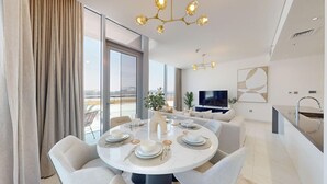 Un comedor moderno con una mesa redonda dispuesta para cuatro personas, un sofá, un televisor y una zona de cocina con un fregadero.