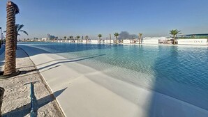 Una gran piscina con agua cristalina y azul, rodeada de palmeras y una playa arenosa.