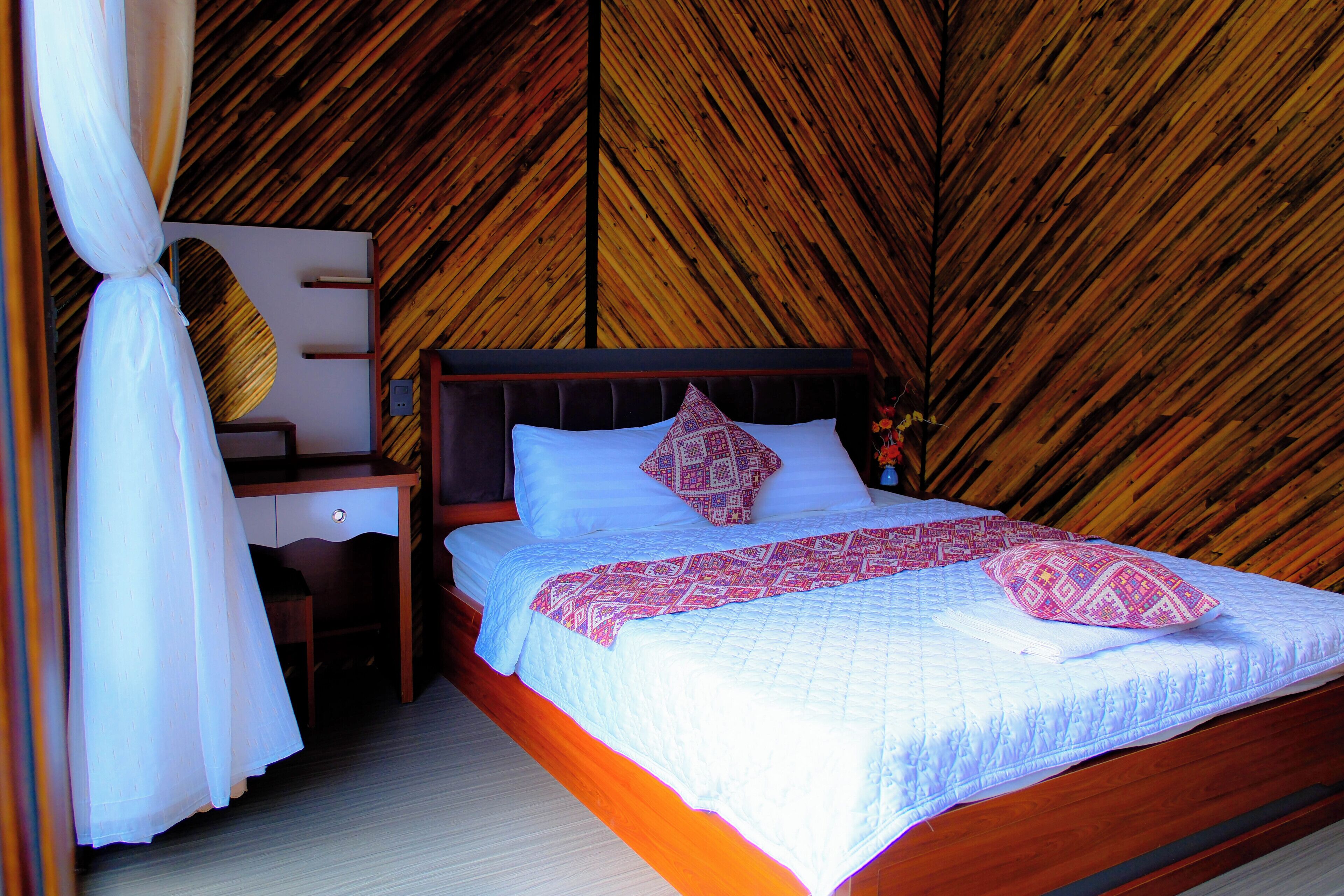 A bedroom with a wooden sloped ceiling, a bed with white bedding and patterned pillows, a nightstand, and a chair.