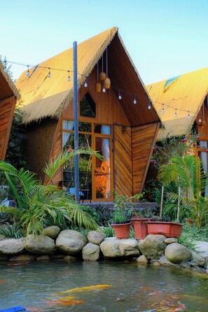 Uma casa de madeira com telhado de palha, um lago com carpas e plantas em vasos.